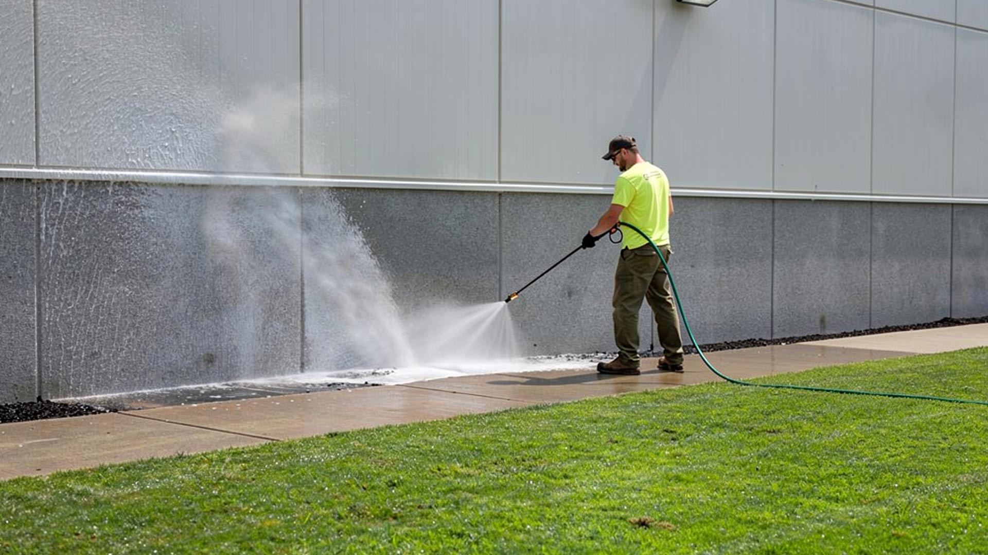 Worker pressure washing the sidewalk and building at an industrial complex